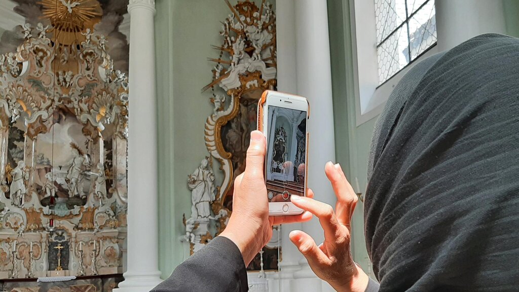 Eine Frau fotografiert mit Ihrem Smartphine einen Kirchenaltar.